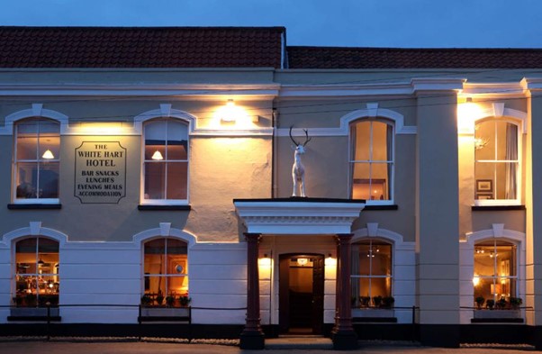 The exterior of the White Hart Hotel in the evening from across the road. The facade is lit up by warm lights