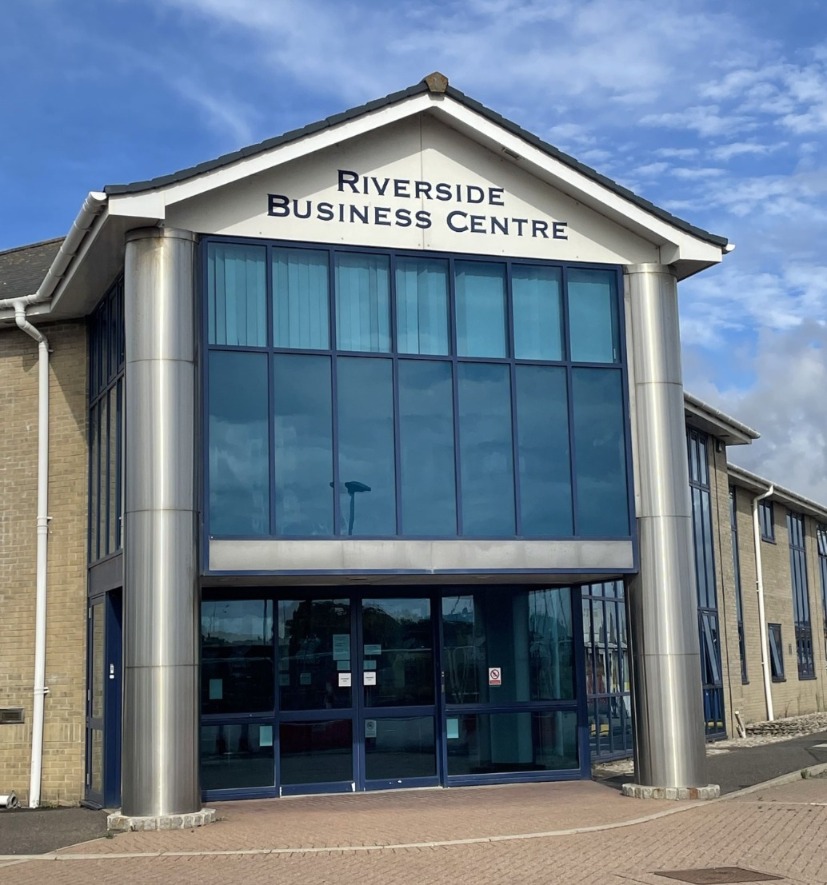 A view of the outside of a large office building with large glass paneled windows with a sign that reads Riverside Business Centre