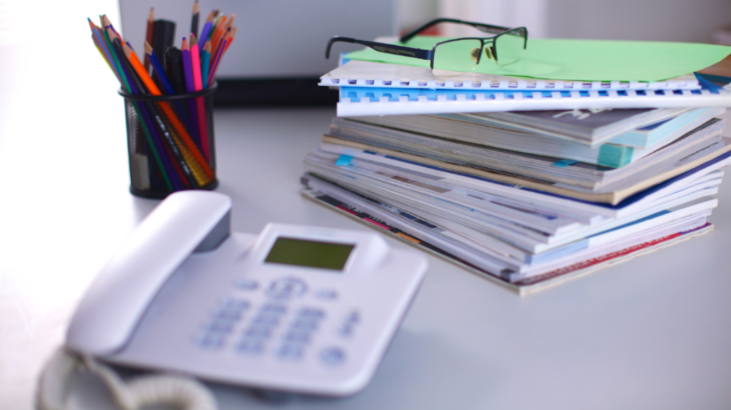 A desk phone, stationary, documents, and a pair of glasses on a desk