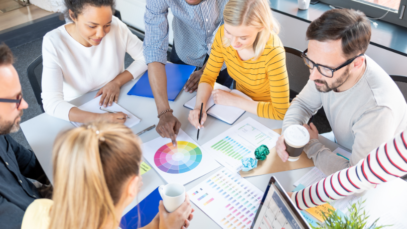 7 people from an in-house marketing team sat around a table discussing colour options for a marketing campaign