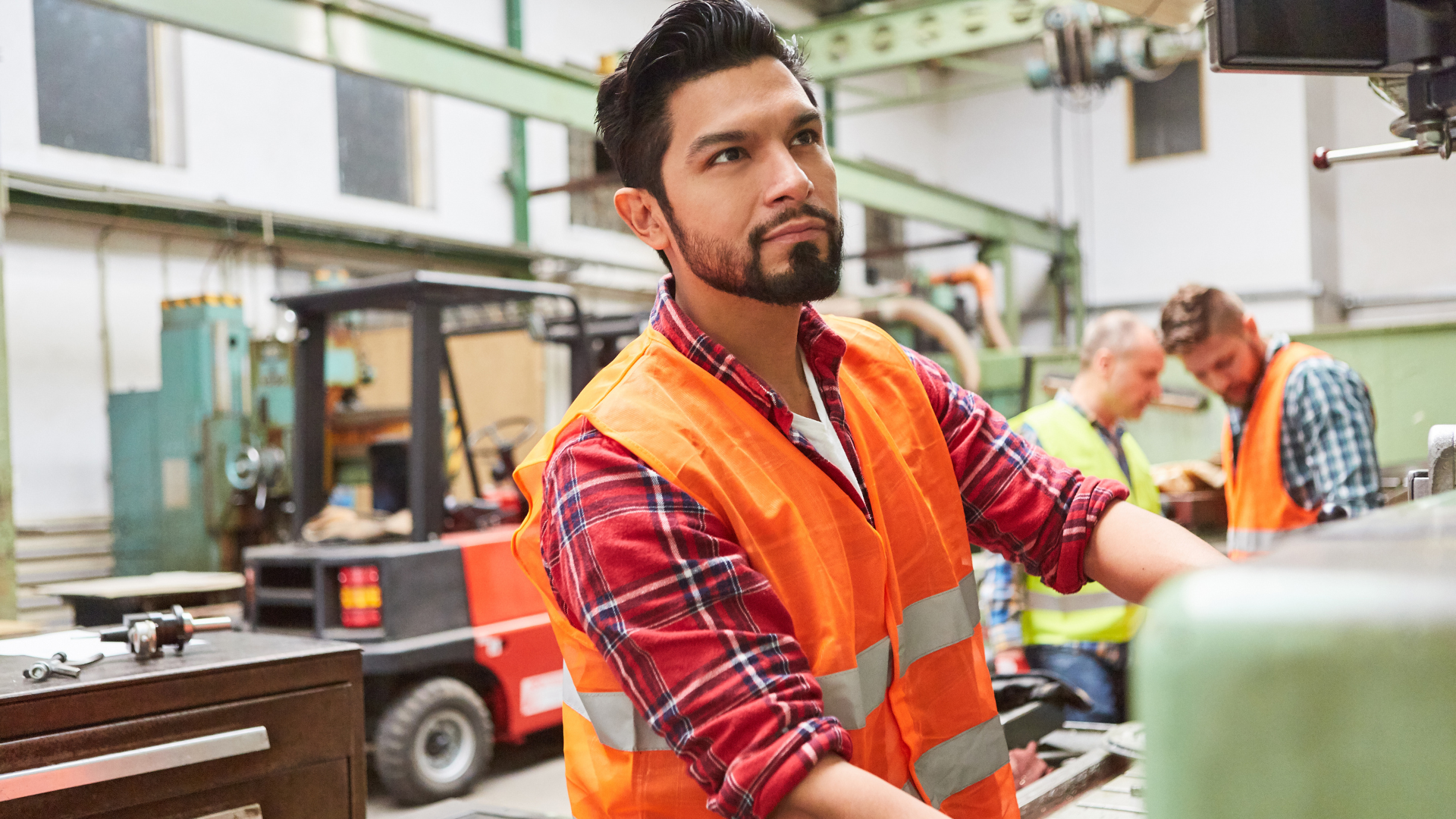 A man in a high-vis vest in a factory with a forklift truck in the background