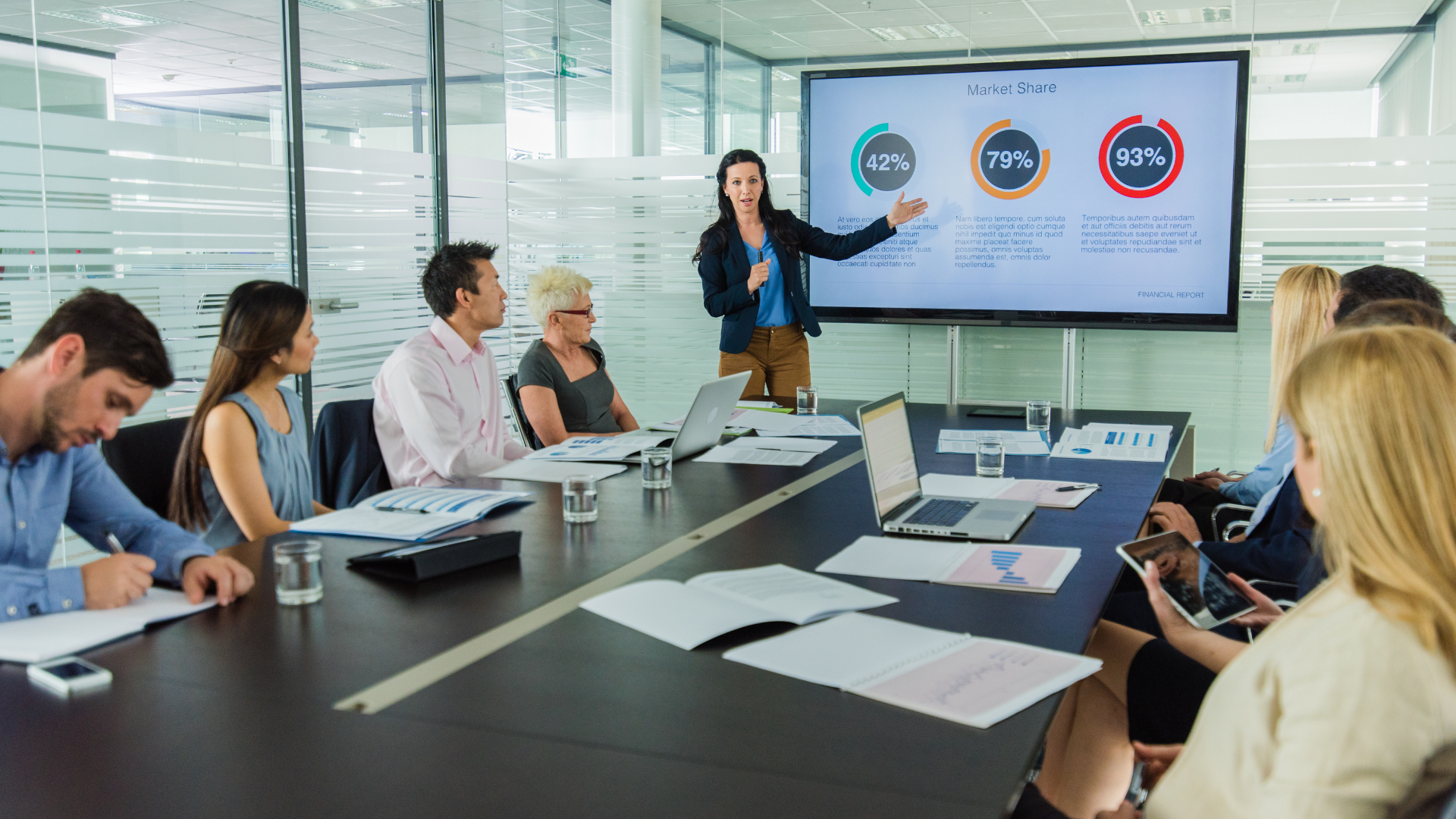 A Marketing Leader giving a presentation about their statistics to a room of people sat at a black table