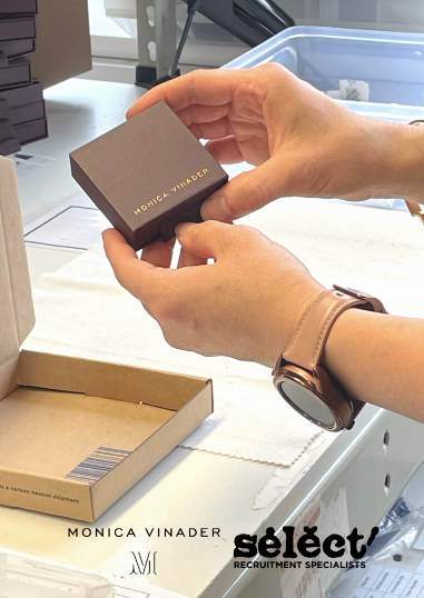 Image shows the close up view of a persons hands holding a purple square box which has Monica Vinader embossed on it, the person is wearing a smart watch