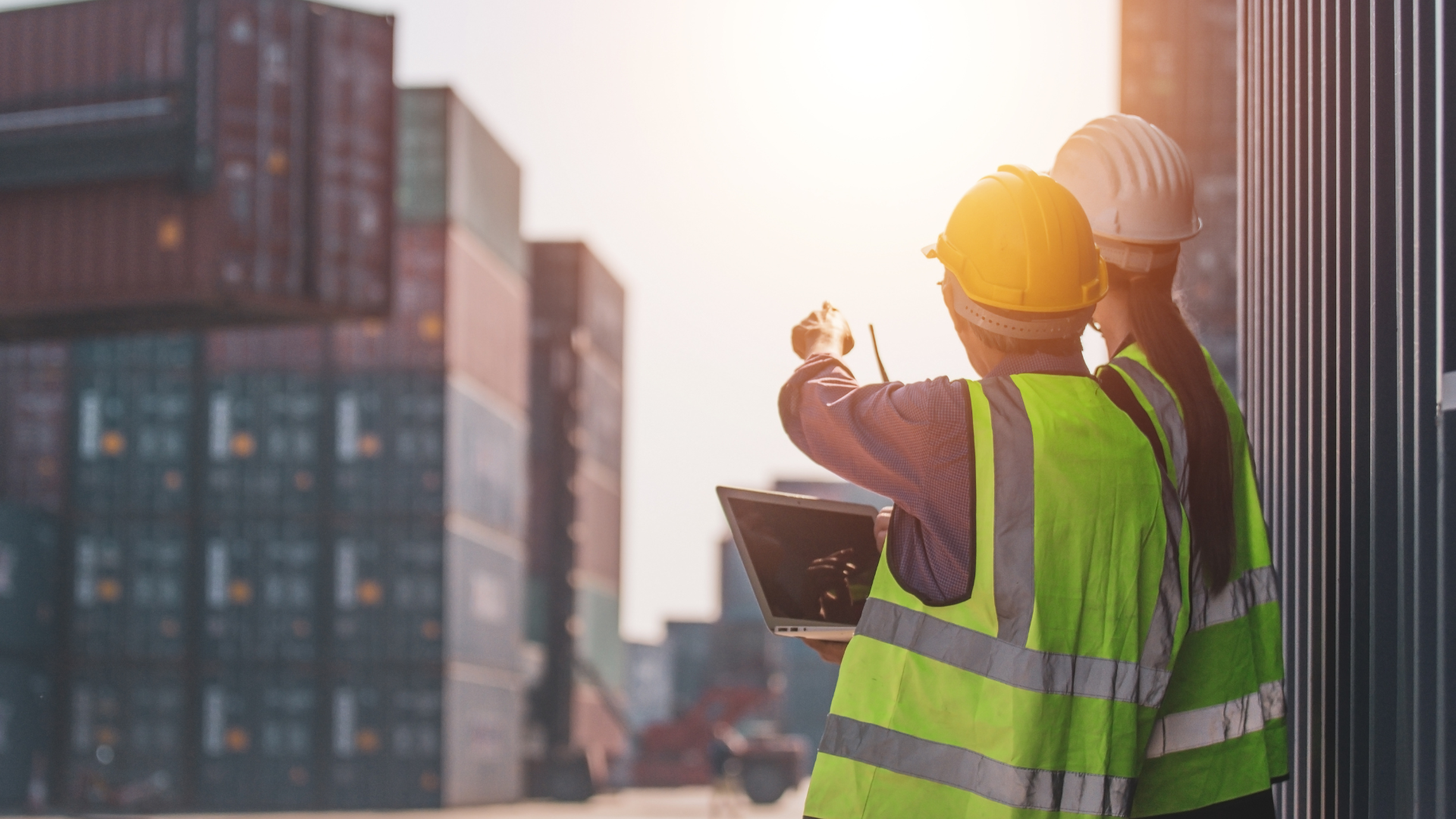 2 workers in hard hats and high-vis vests looking at freight containers