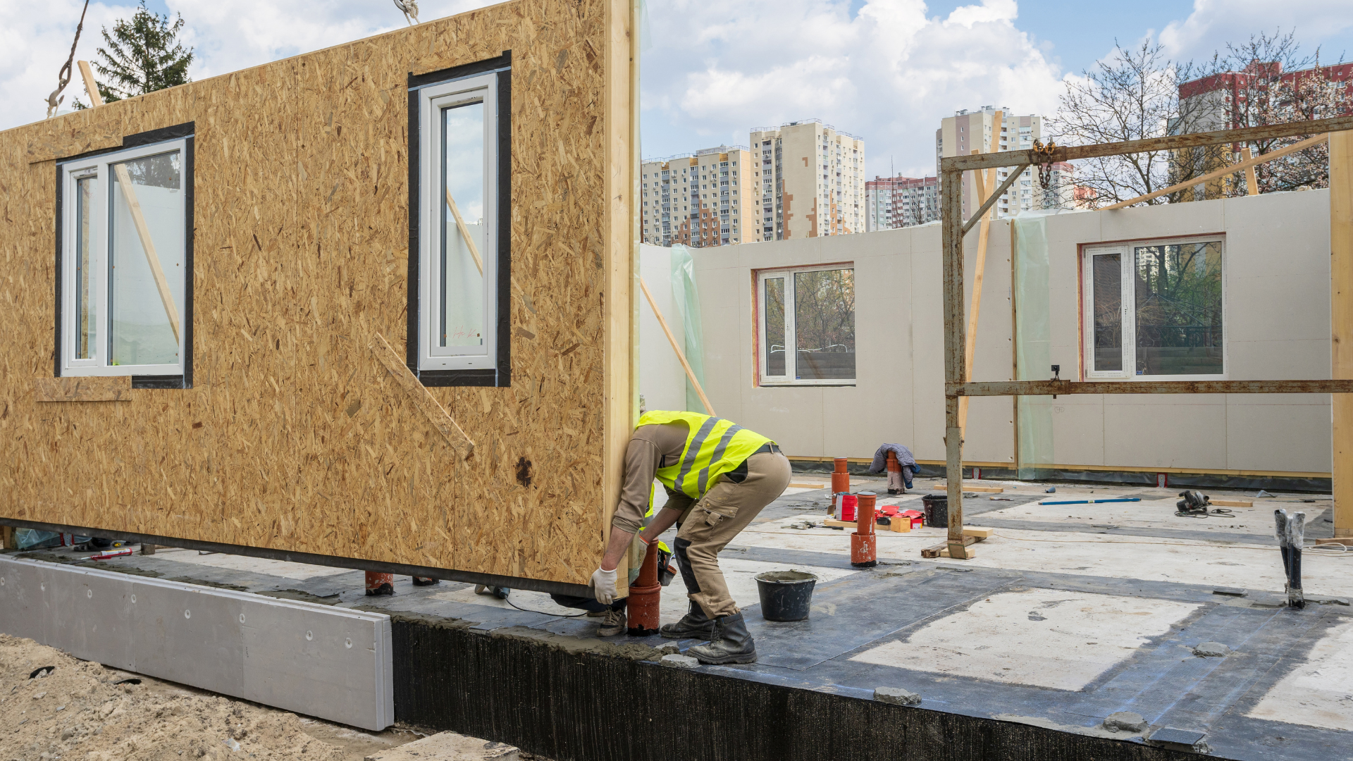 A construction worker installing a modular piece of a wall on to the frame of the building with the assistance of a crane