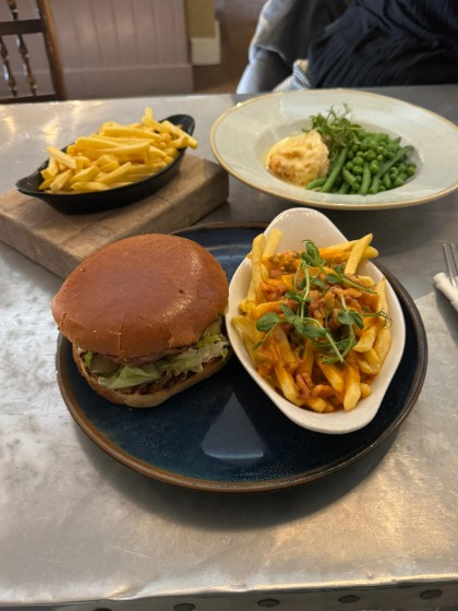 A bowl of chips and a cheeseburger on a black plate. Another bowl of chips and a plate with a cheese souffle and vegetables sit alongside the first plate on a table