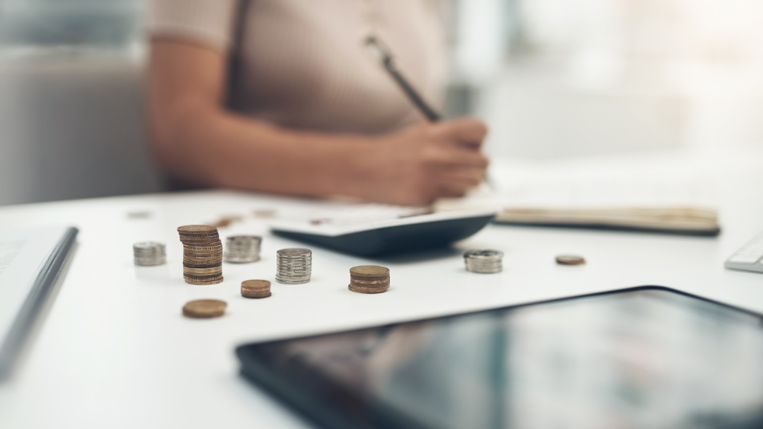 A calculator and coins on a desk, with a payroll professional in the background