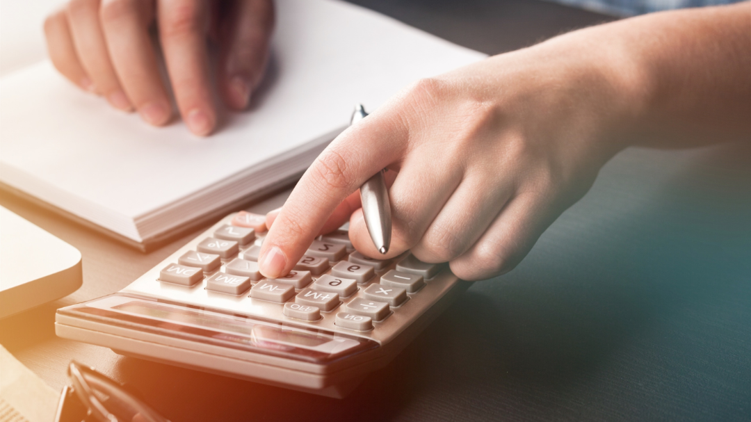 A person using a calculator on a desk with a notepad