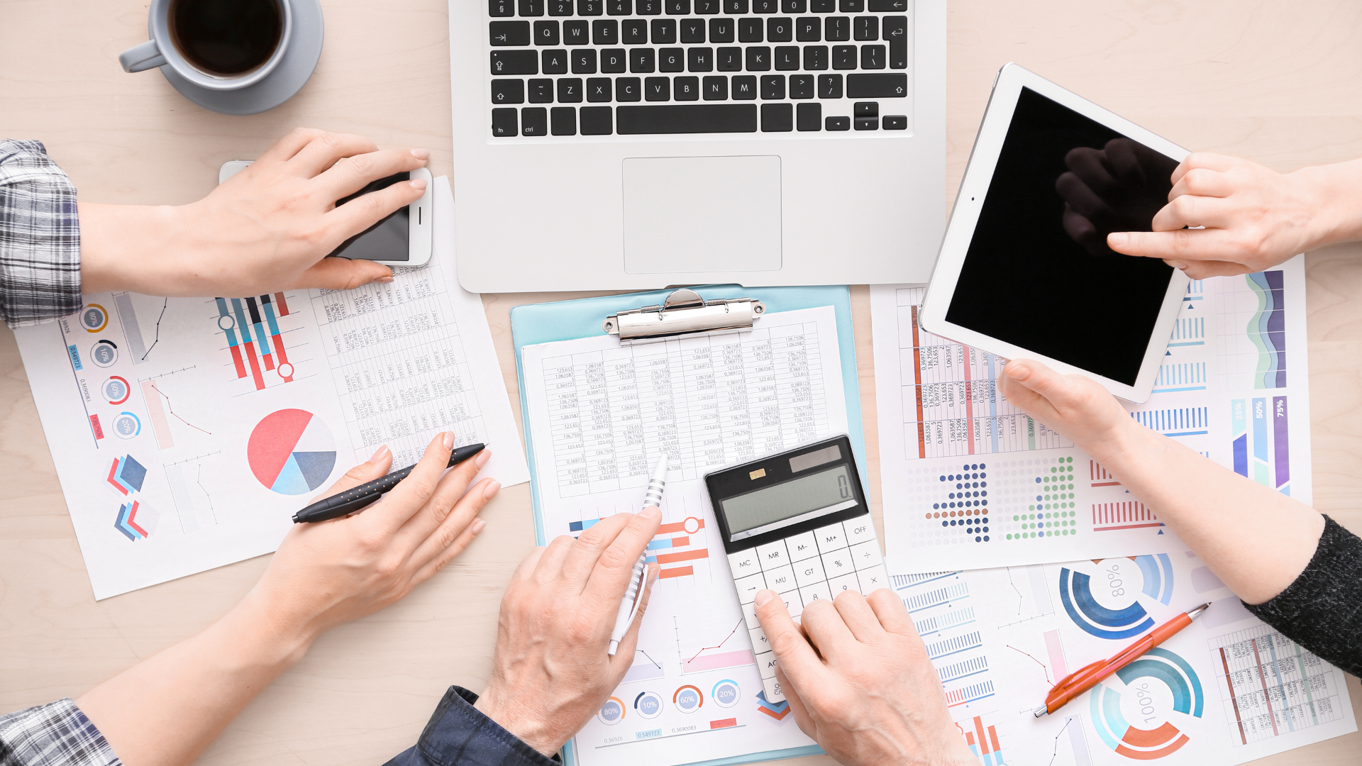 Several people collaborating on accounting data, using a laptop, calculator, and tablet