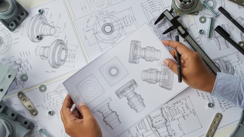 An overhead image of a person looking at technical engineering drawings on a desk