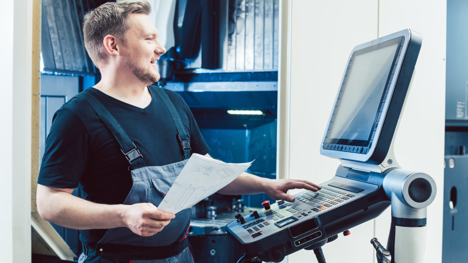 A close-up image of a CNC machine. The machine has multiple drill-bits of different gauges. They are currently stationary, above a piece of metal that is ready to be milled.