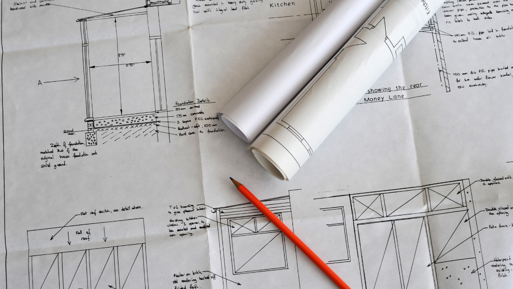 An image of architectural drawings on white paper. There is an orange pencil on top of the page