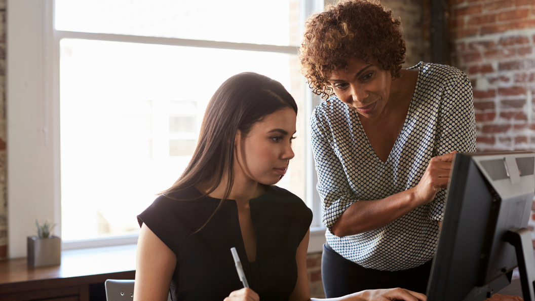 An image of a manager helping a worker with a task on a computer