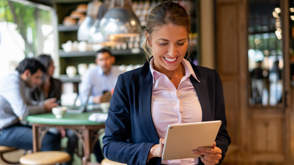 An image of a restaurant manager looking at data on a tablet. She is wearing a pink shirt and navy-blue blazer