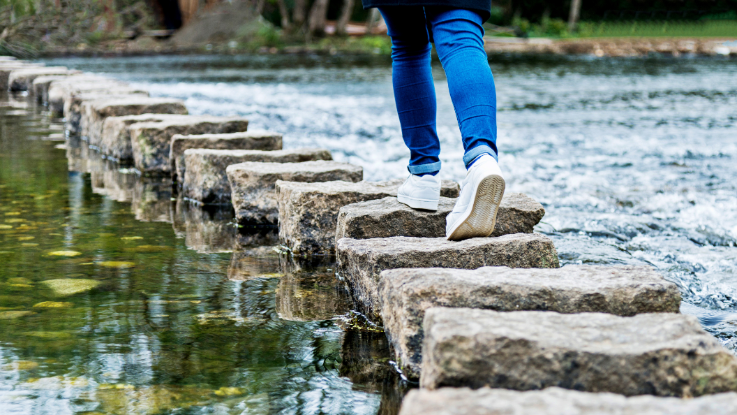 An image of a person walking across stepping-stones across a stream of water