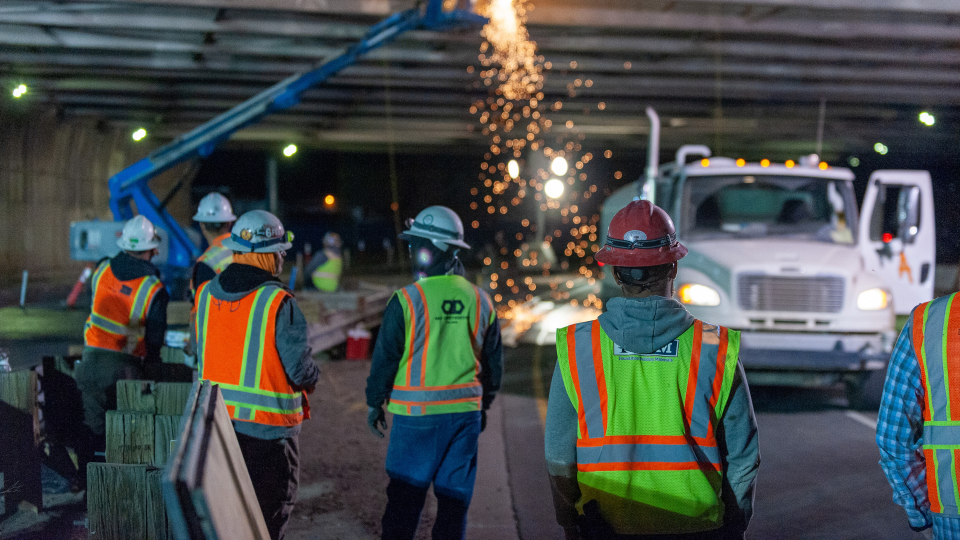 An image of construction workers working on a road late at night