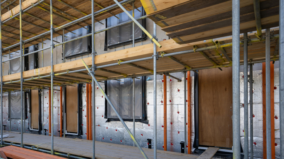 An image of a building under construction. The outer walls are covering in insulation, and there is scaffolding in front of the building