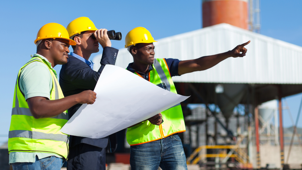 An image of three construction workers looking at a project and discussing blueprints