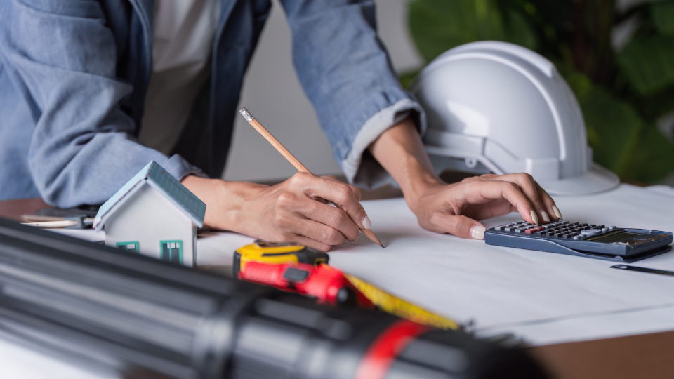 An image of a structural engineer working on construction designs. She is using a pencil and a calculator to make adjustments.