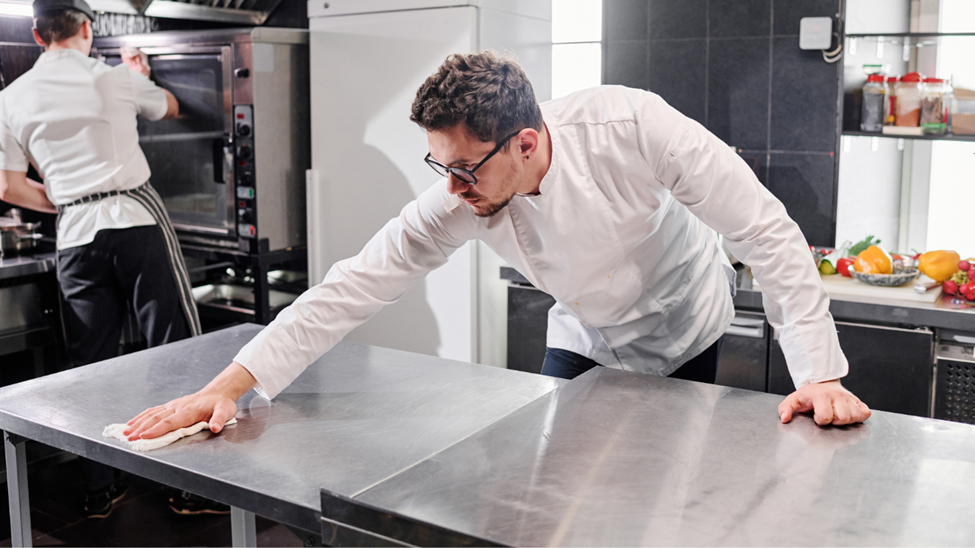 A kitchen assistant cleaning work surfaces in a commercial kitchen