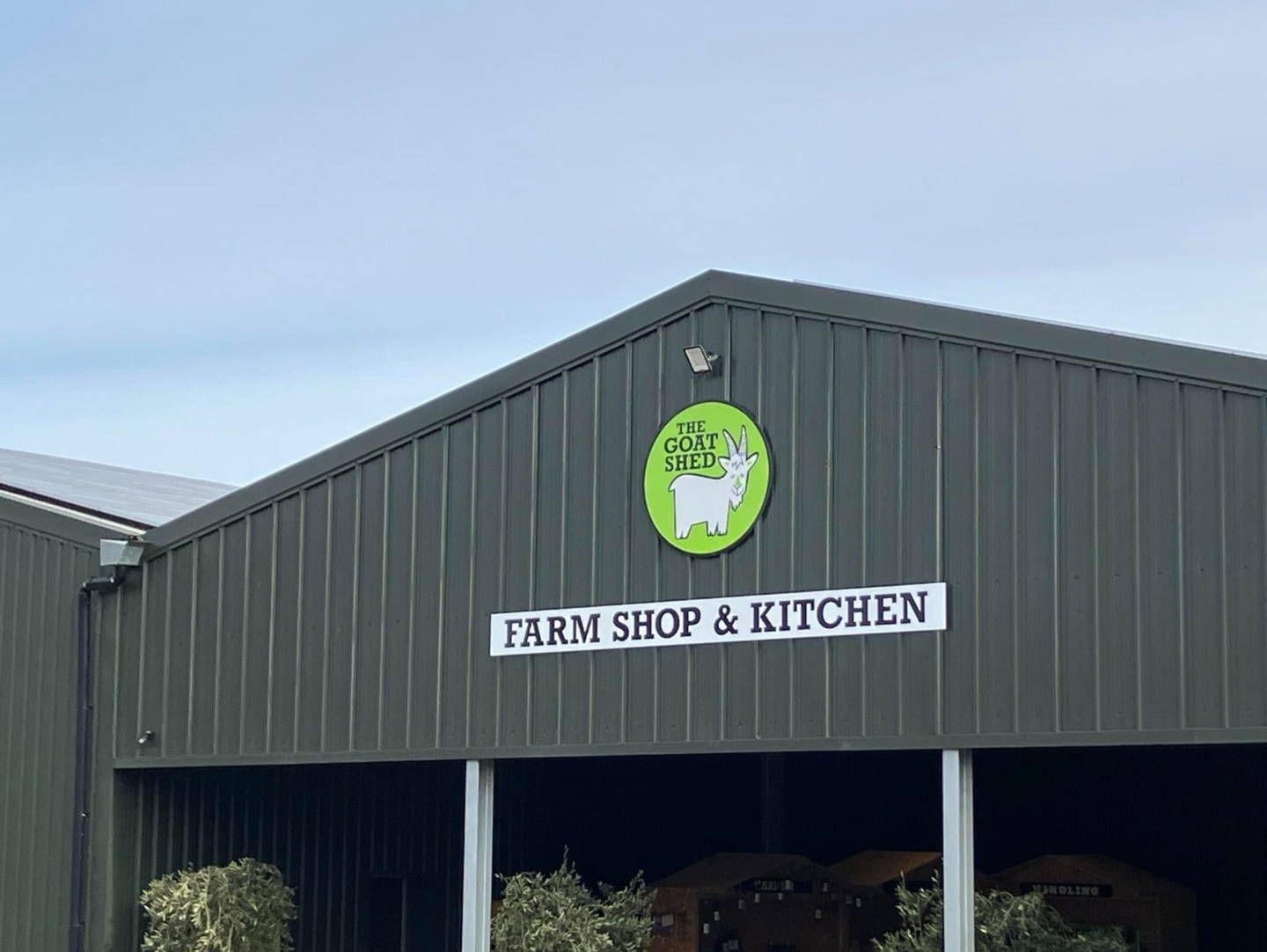 The roof of The Goat Shed farm shop. The roof is dark green and triangular. The Goat Shed logo is on there, a white goat in a green circle