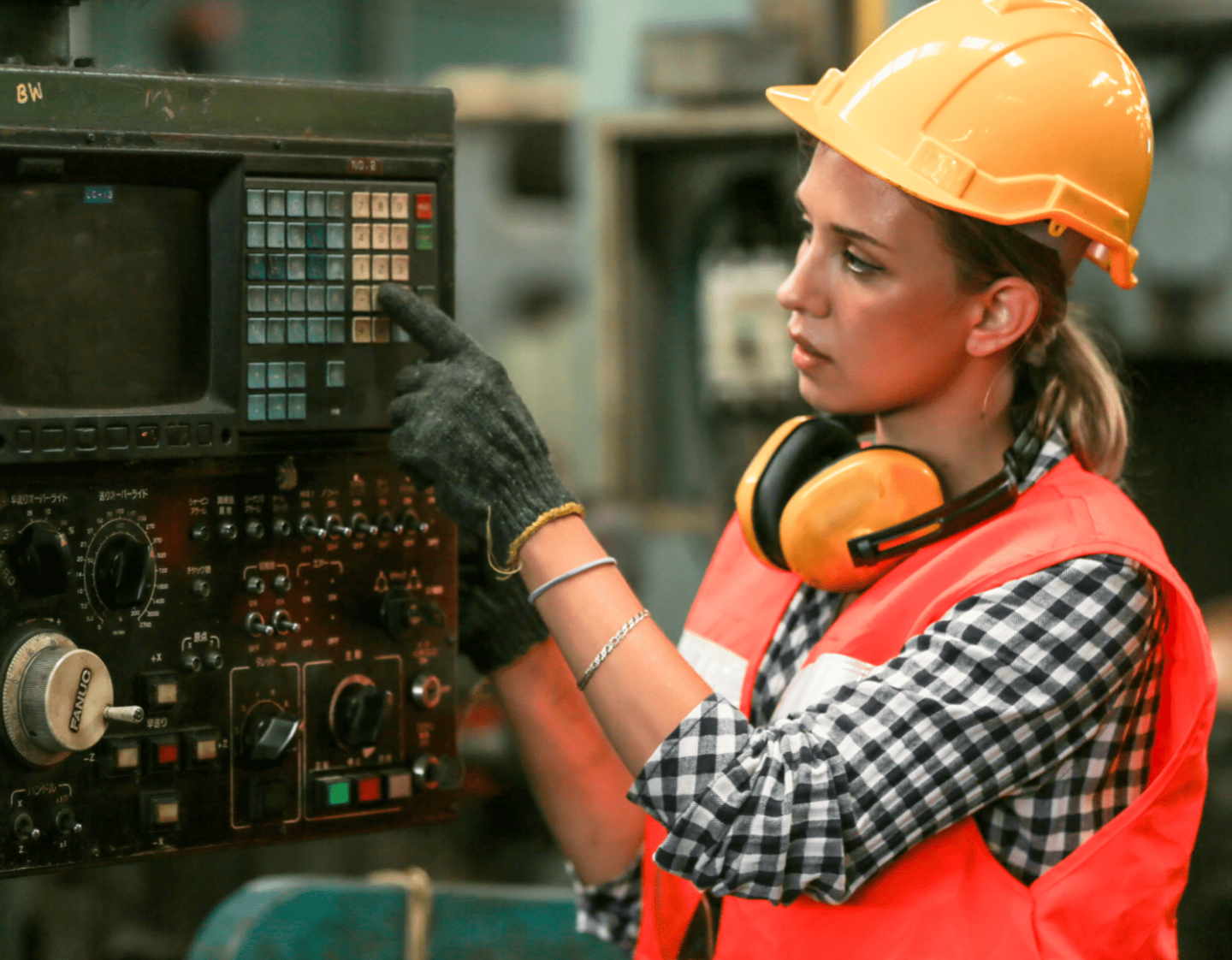 A woman in a high viz jacket and safety gear using a programmable production machine