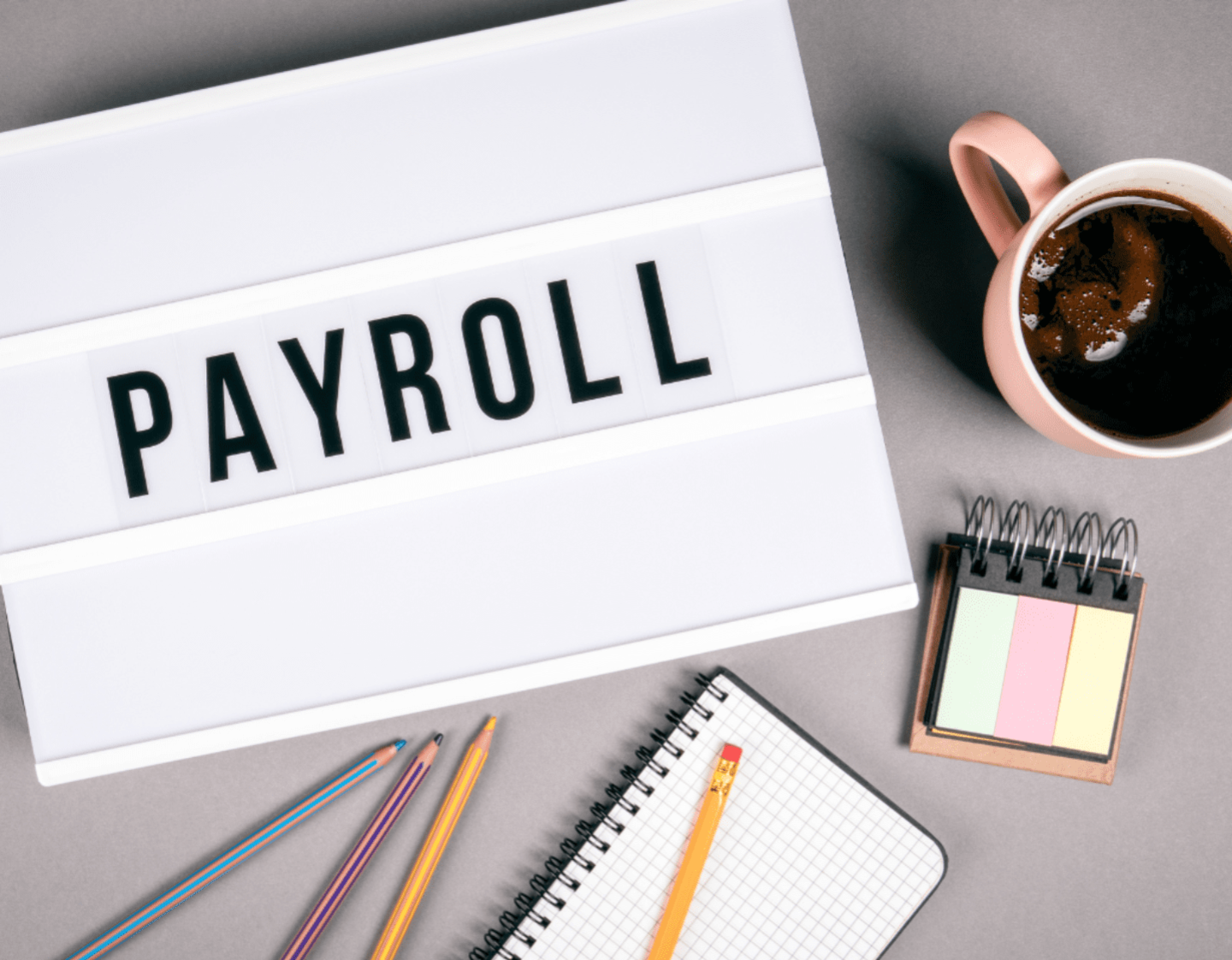 A lightbox with the word "Payroll" on it, on a desk with a coffee cup and stationairy 