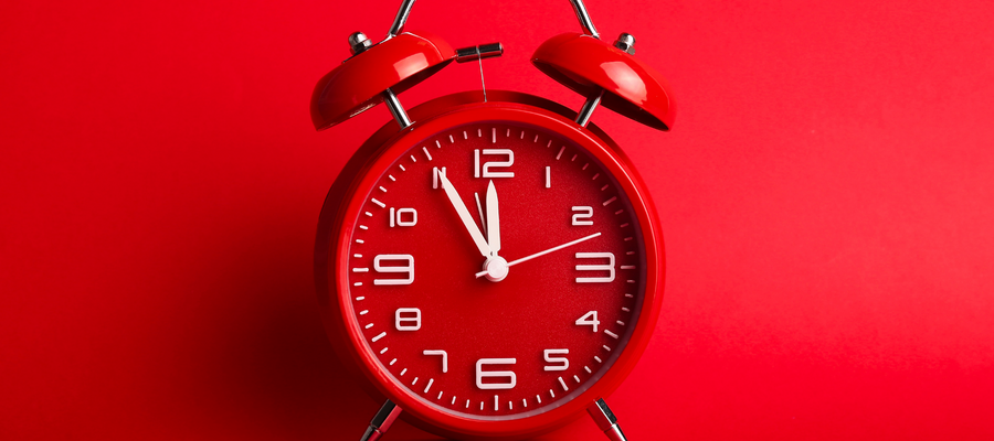 An image of a red alarm clock with white numbers and white hands against a red background