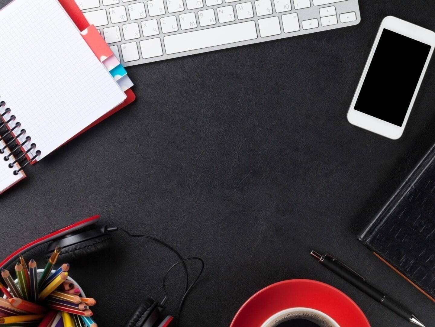 A keyboard, notepad, smartphone, and headset on a black leather desk