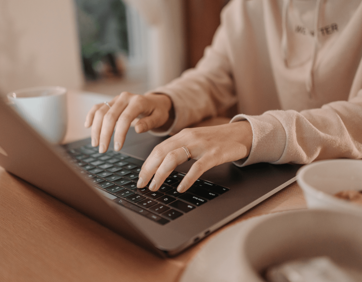 An image of a person writing content on their laptop. They are wearing casual clothing and the laptop is on a brown wooden desk