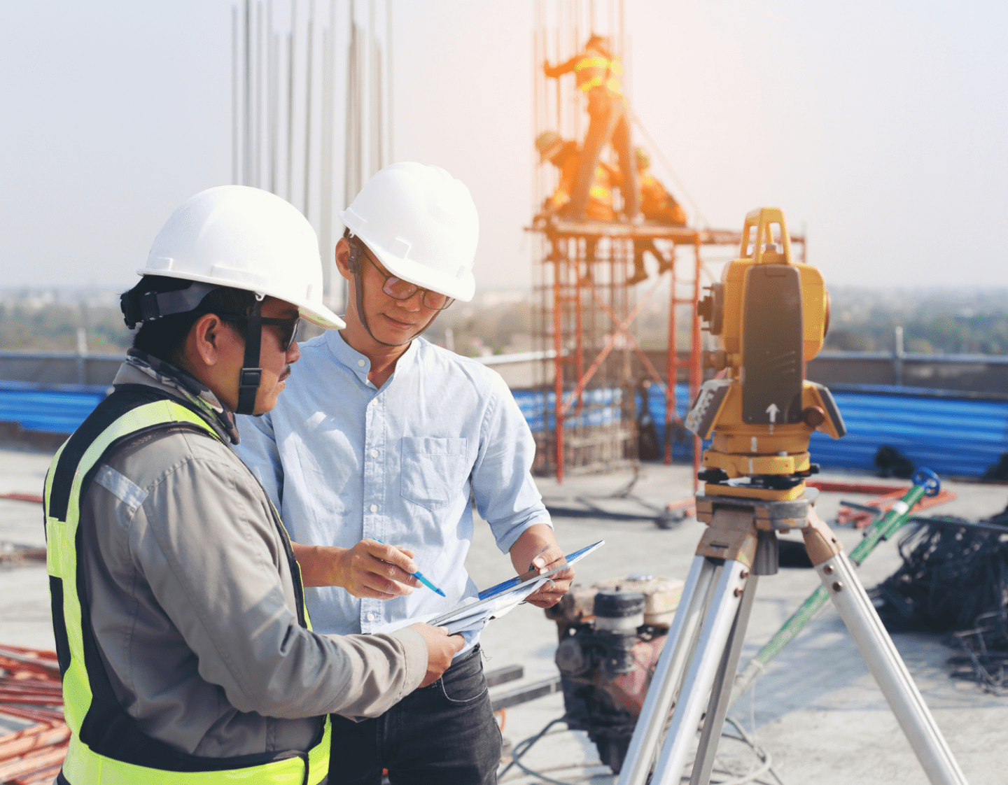 An image of two people on a construction site, looking at data. They are stood on top of a building under construction, looking at a clipboard