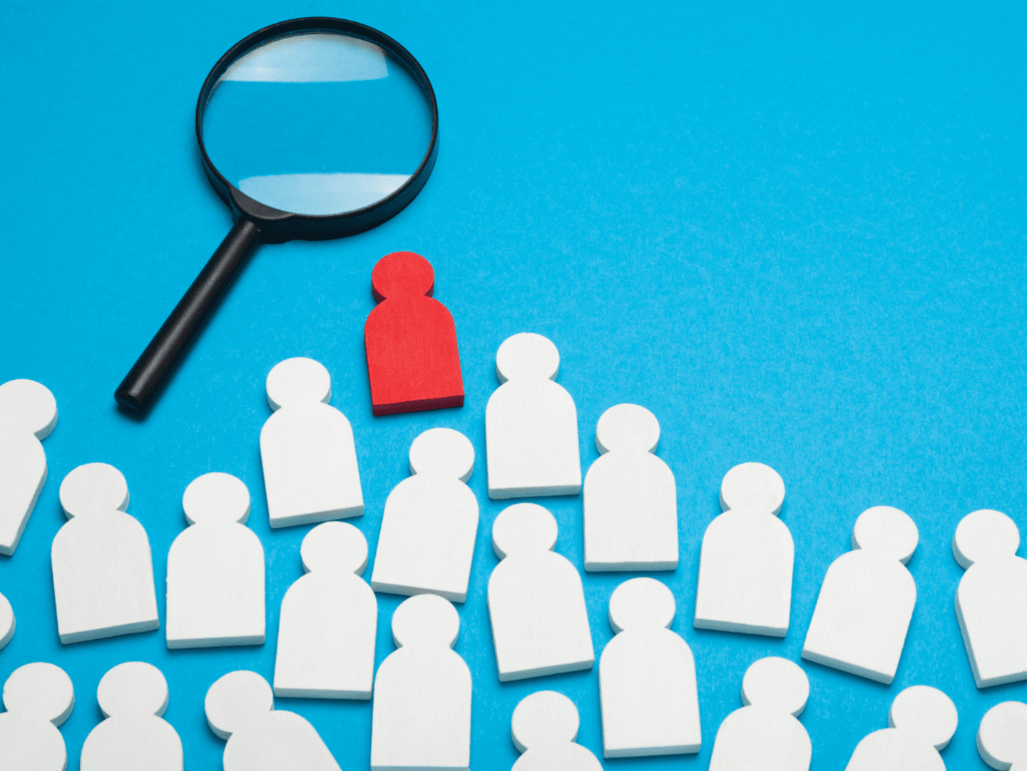 An image showing white wooden figures on a blue background. There is one red figure at the top of the pile, and a magnifying glass next to it.