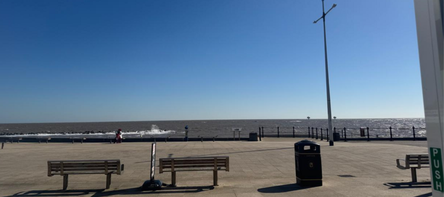 An image of Lowestoft seafront, featuring benches, signs, and the sea