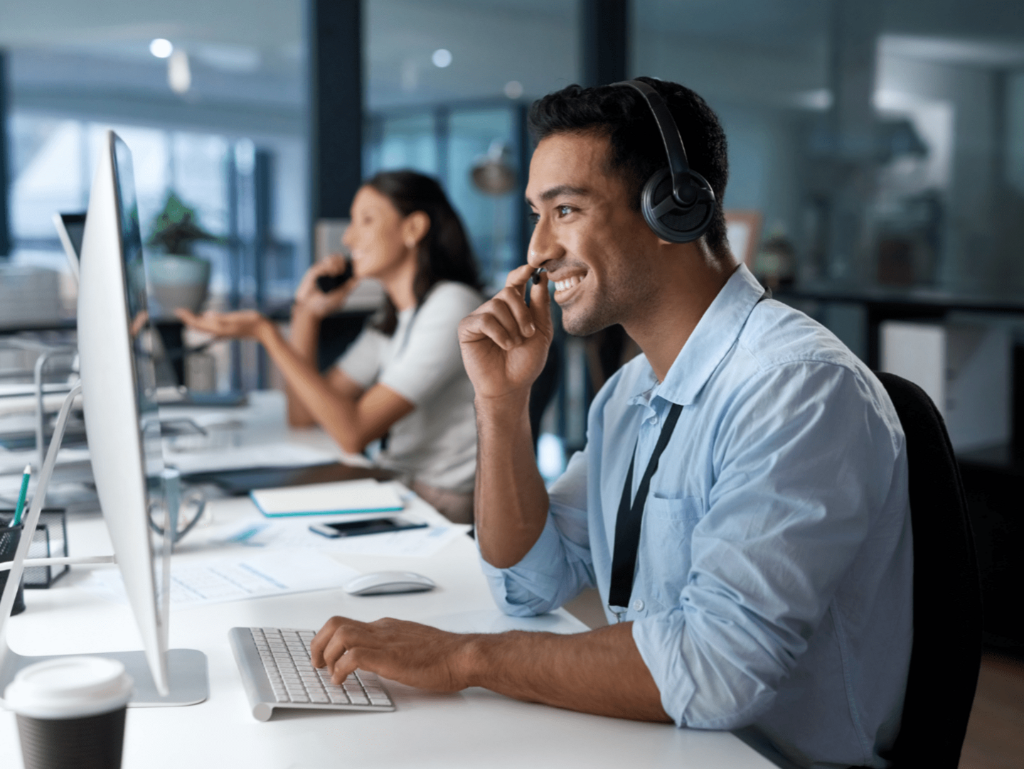 An image of two customer service agents working. They are sat at desks and are wearing headsets